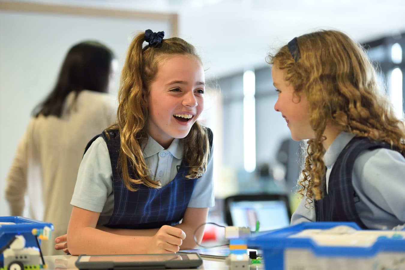 Two young school girls sitting at a desk and laughing with each other