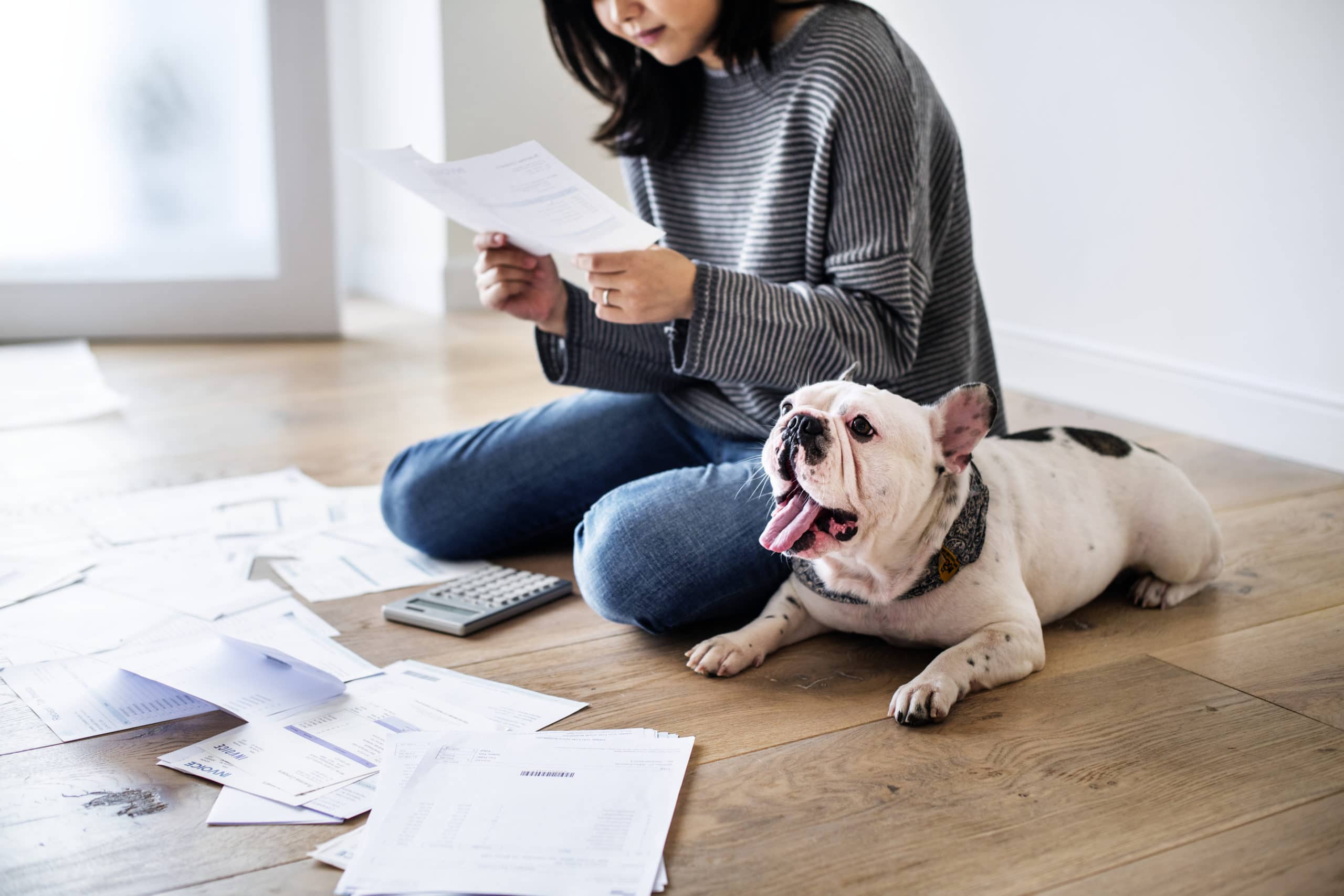 Woman sitting on ground with bills in front of her. She has a dog to her left and she is 'managing her debts'