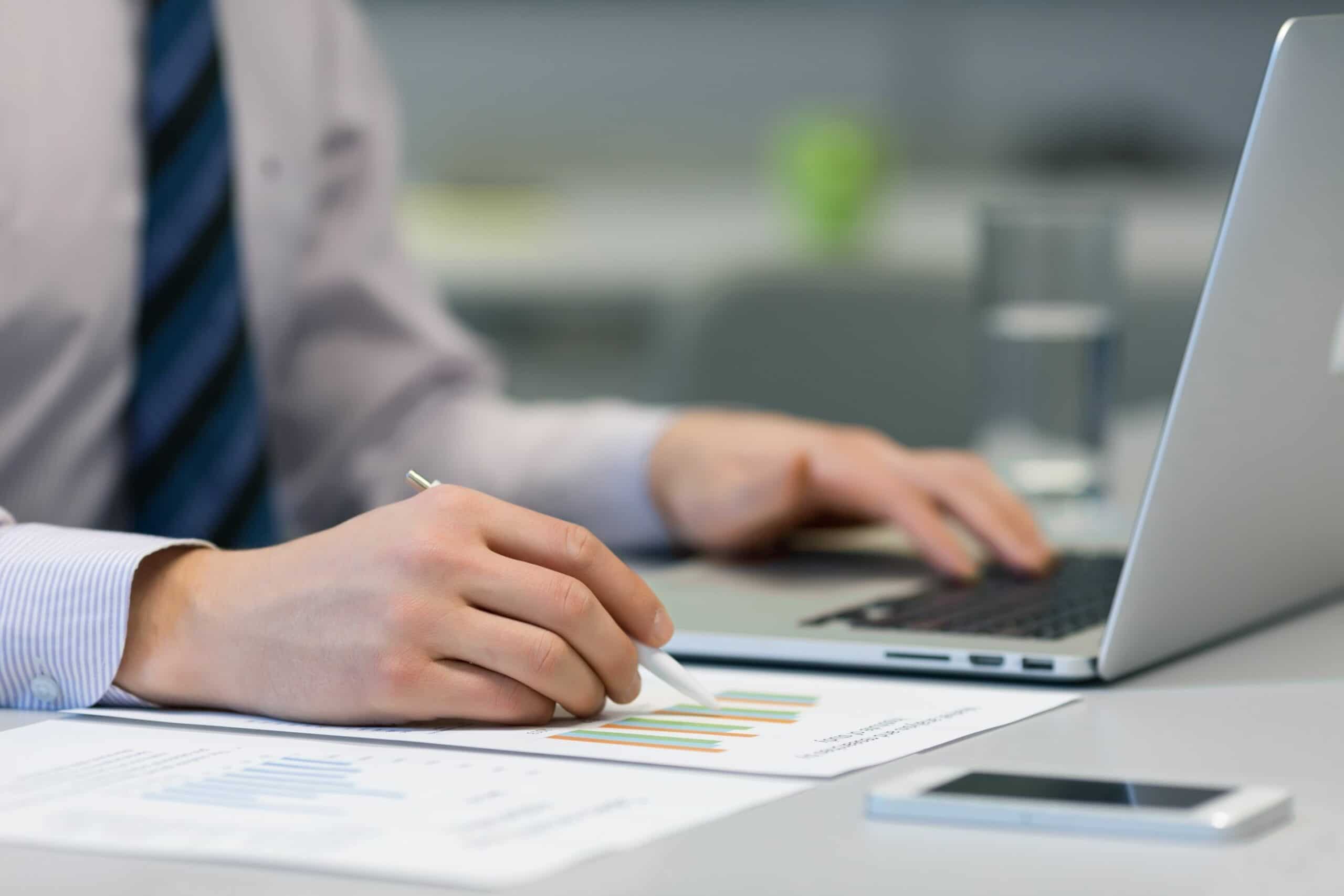 Cropped image of business man working on laptop alongside paperwork on desk.