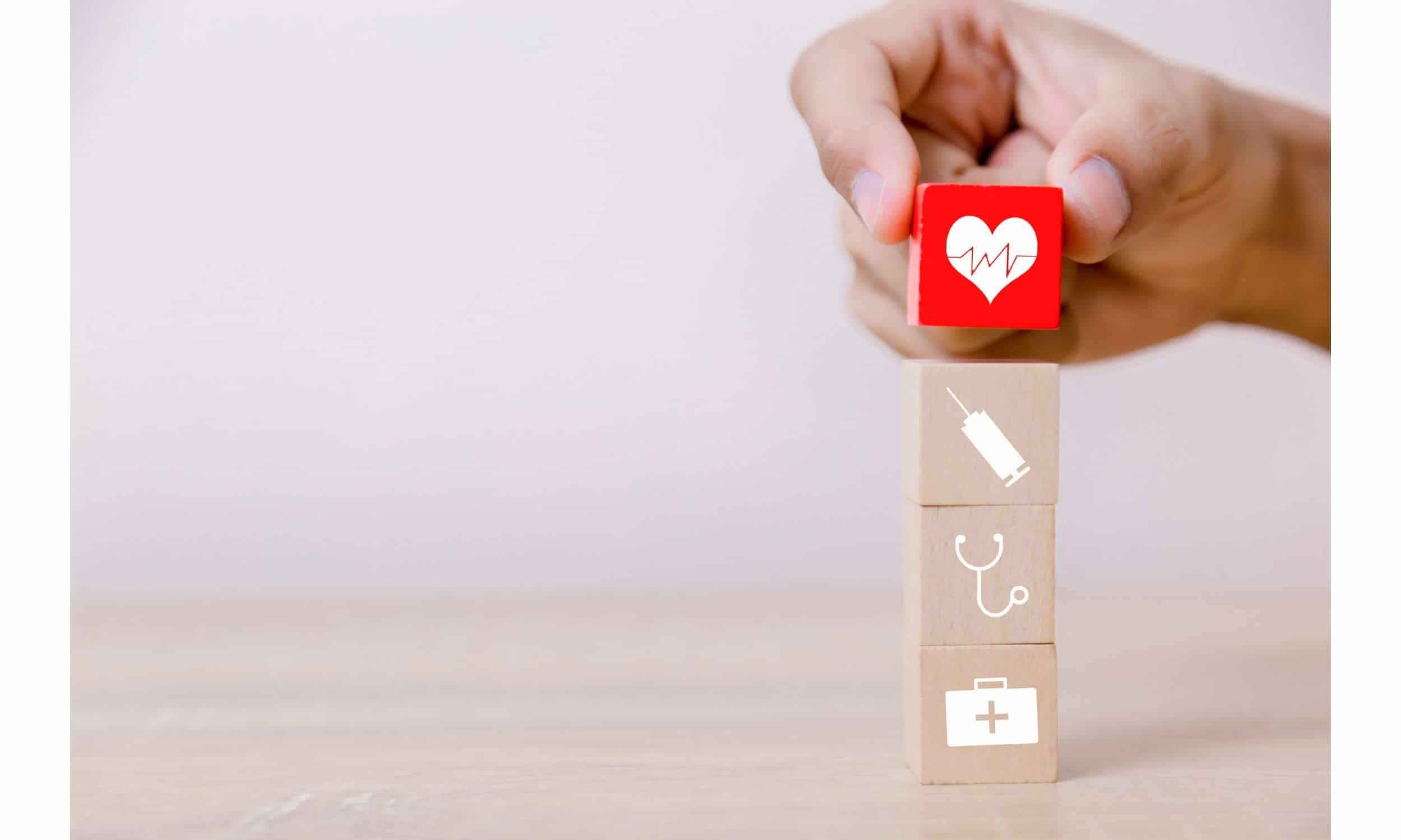 Hand arranging wood block with healthcare symbol on top of three wooden blocks.