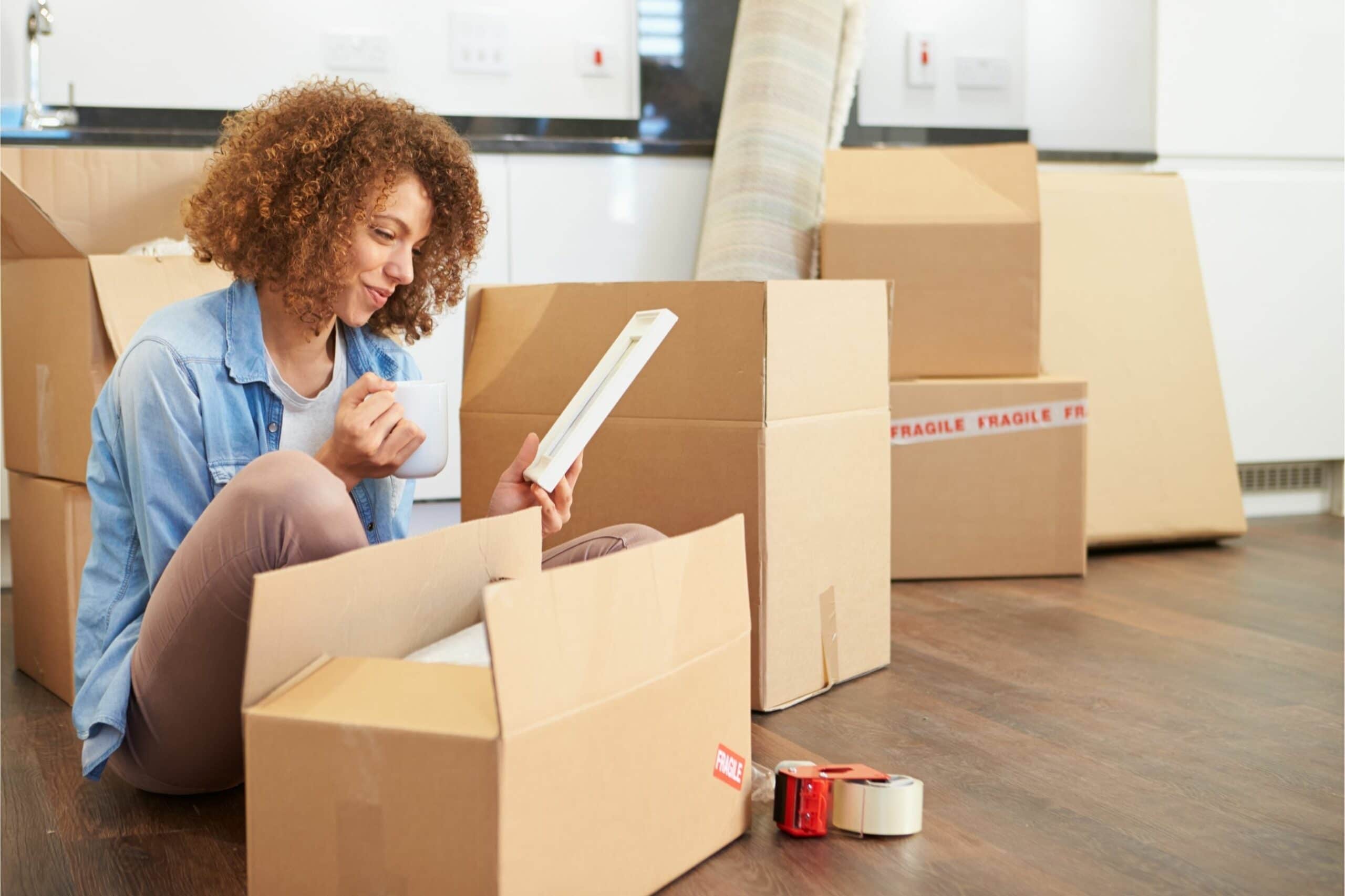 Woman sitting on floor surrouned by moving boxes.