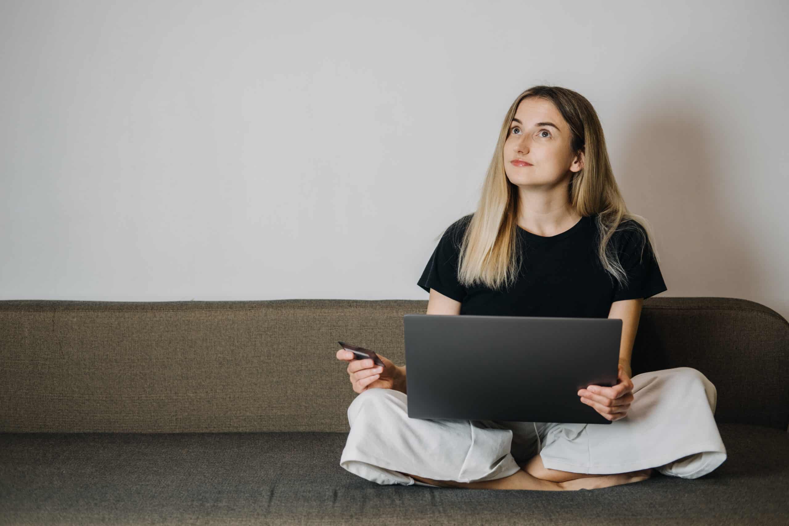 Impulse Buying, Online Shopping, fast fashion, shopaholic, spending money concept. Young woman at home holding credit card and using laptop computer and cell phone.