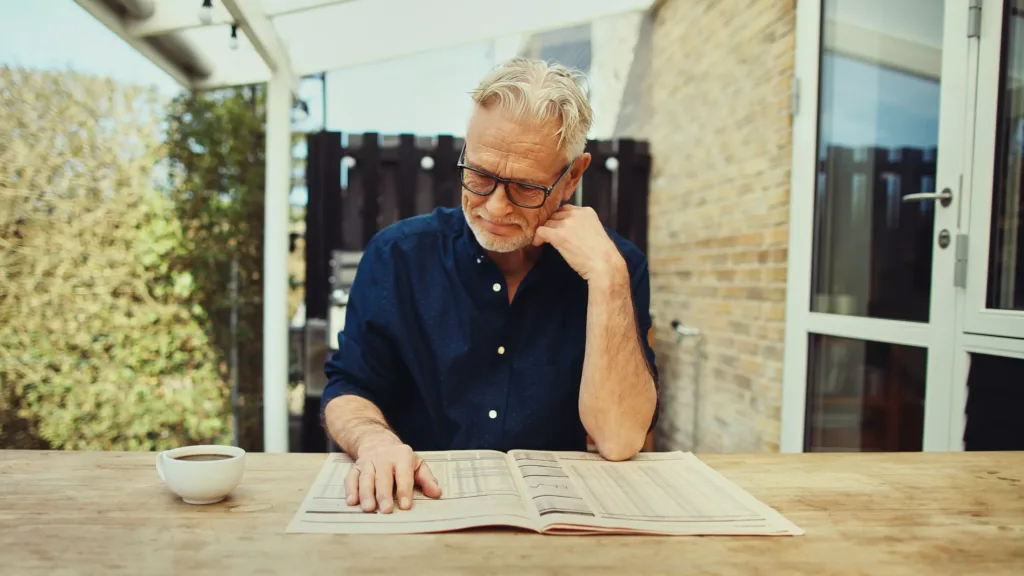 Smiling senior man reading a newspaper outside on his patio
