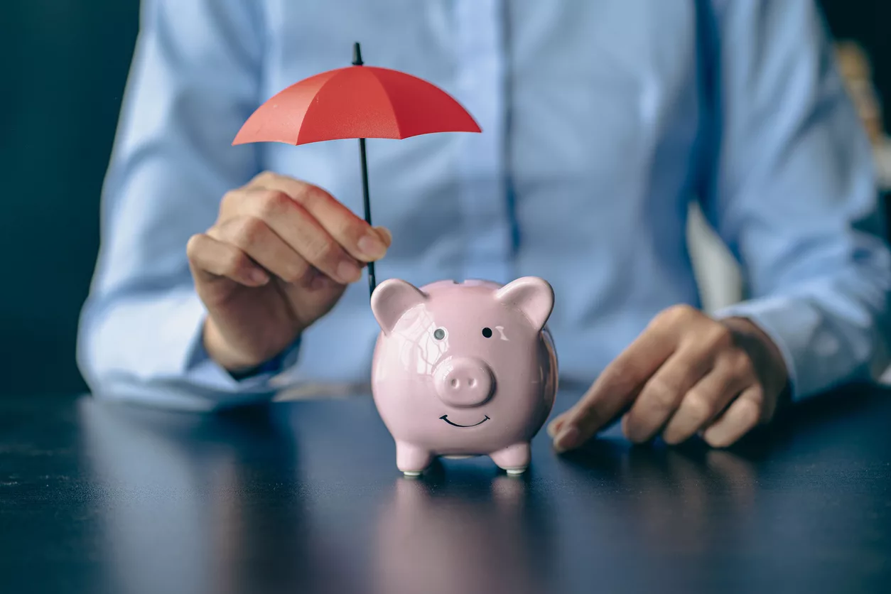 Piggy bank and woman holding red umbrella Protect assets and save money on health insurance purchases.Woman holding small umbrella over piggy bank against beige background, closeup
